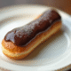 Éclair au chocolat sur une assiette blanche en gros plan
